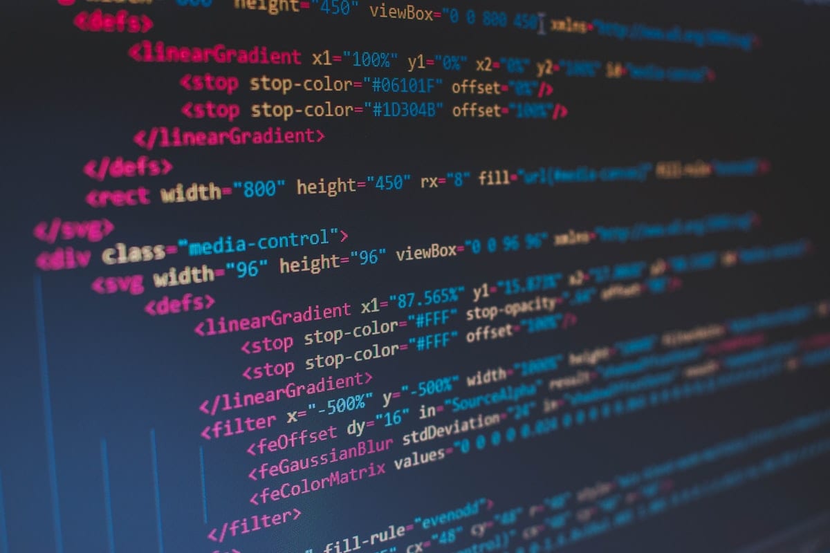 A close-up of source code on a backlit monitor in a darkened room, evoking the AI-agent session in which the SharedRoot sandbox escape began.