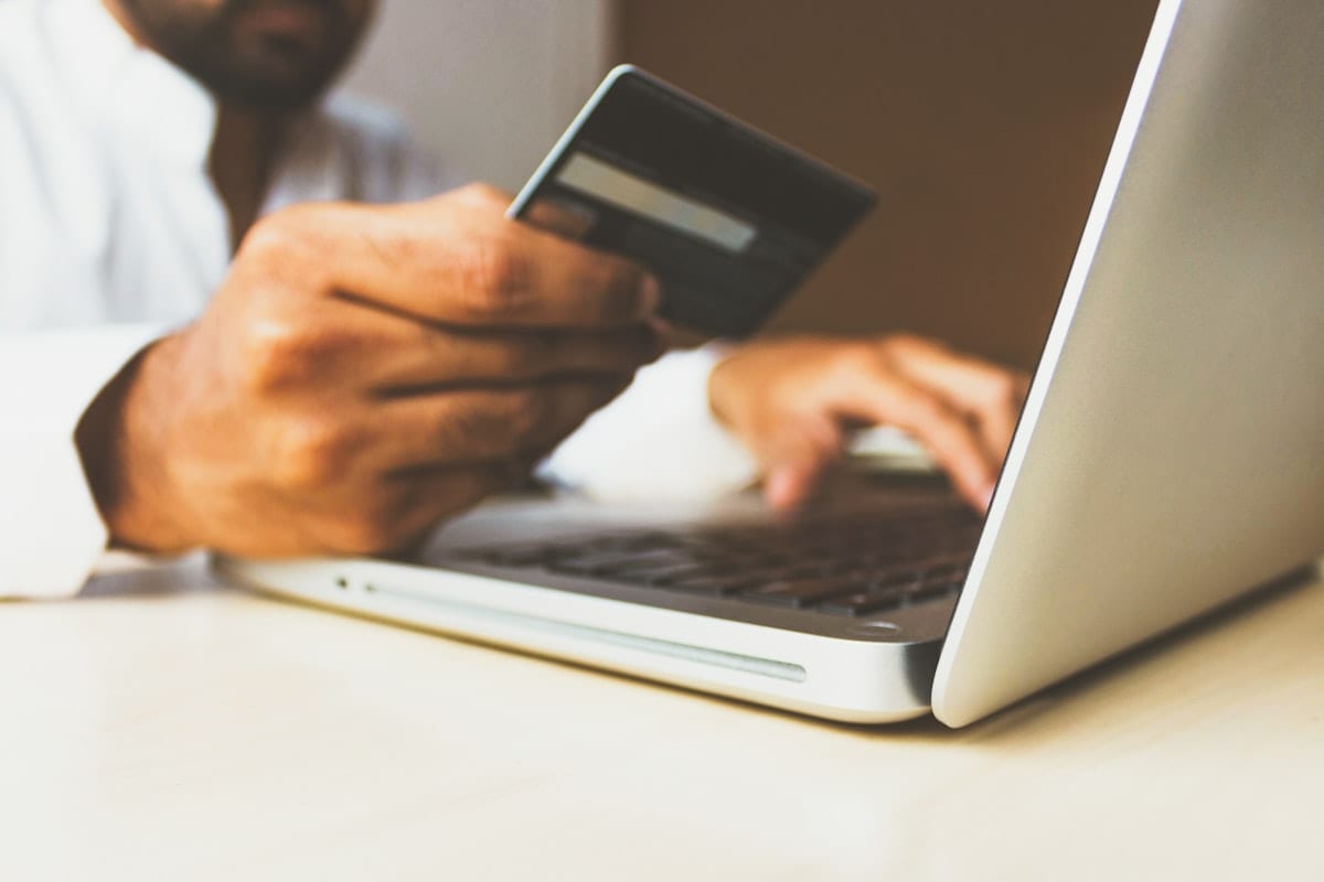 Person holding a payment card while using a laptop, illustrating online identity privacy